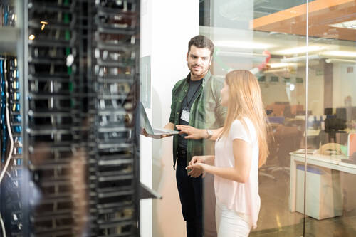 Two business people standing server room with laptop discussing